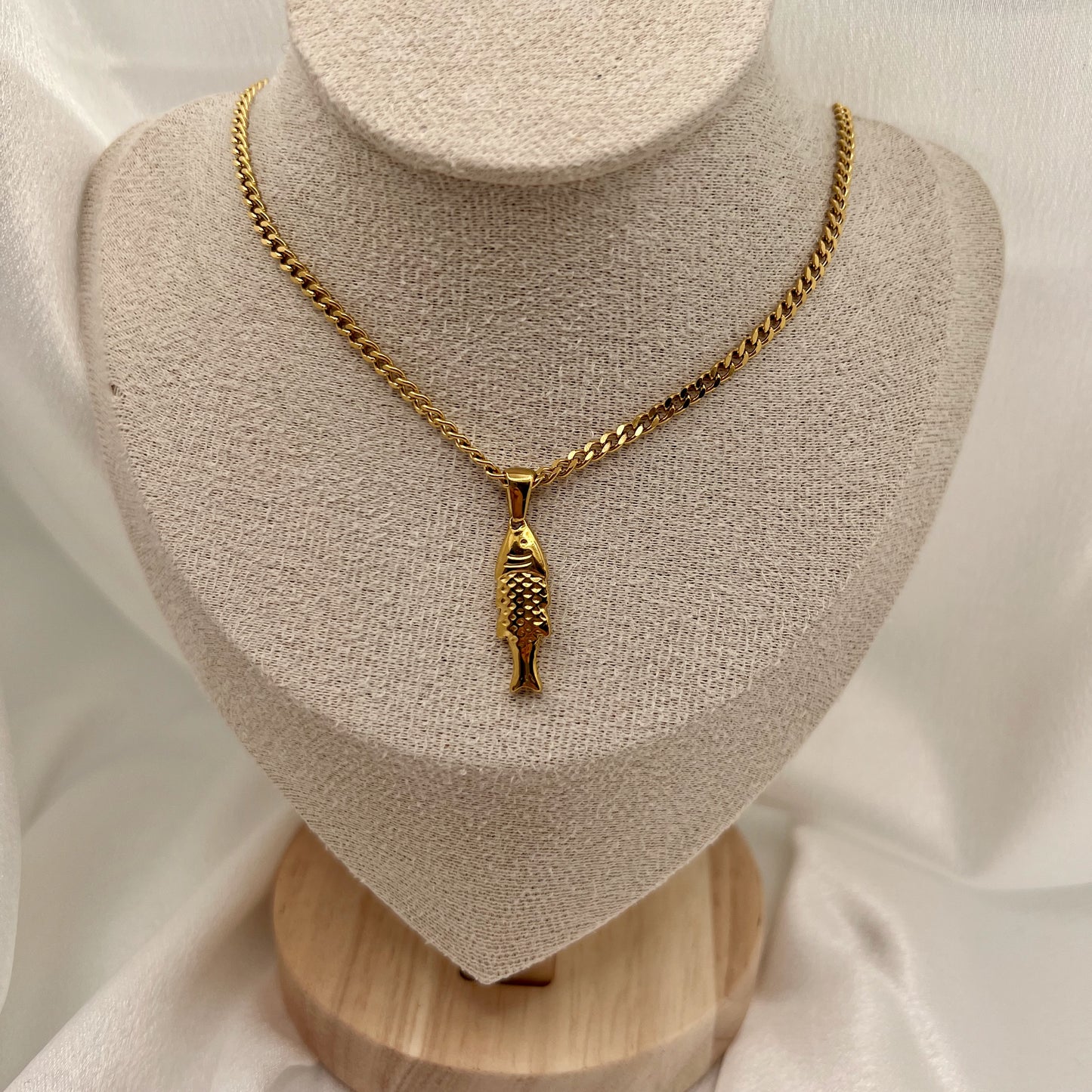 Gold chain necklace with a fish pendant on a mannequin bust.