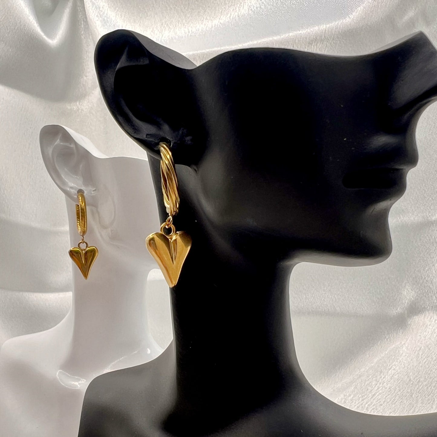 Gold heart-shaped earrings on a black mannequin against a white satin background