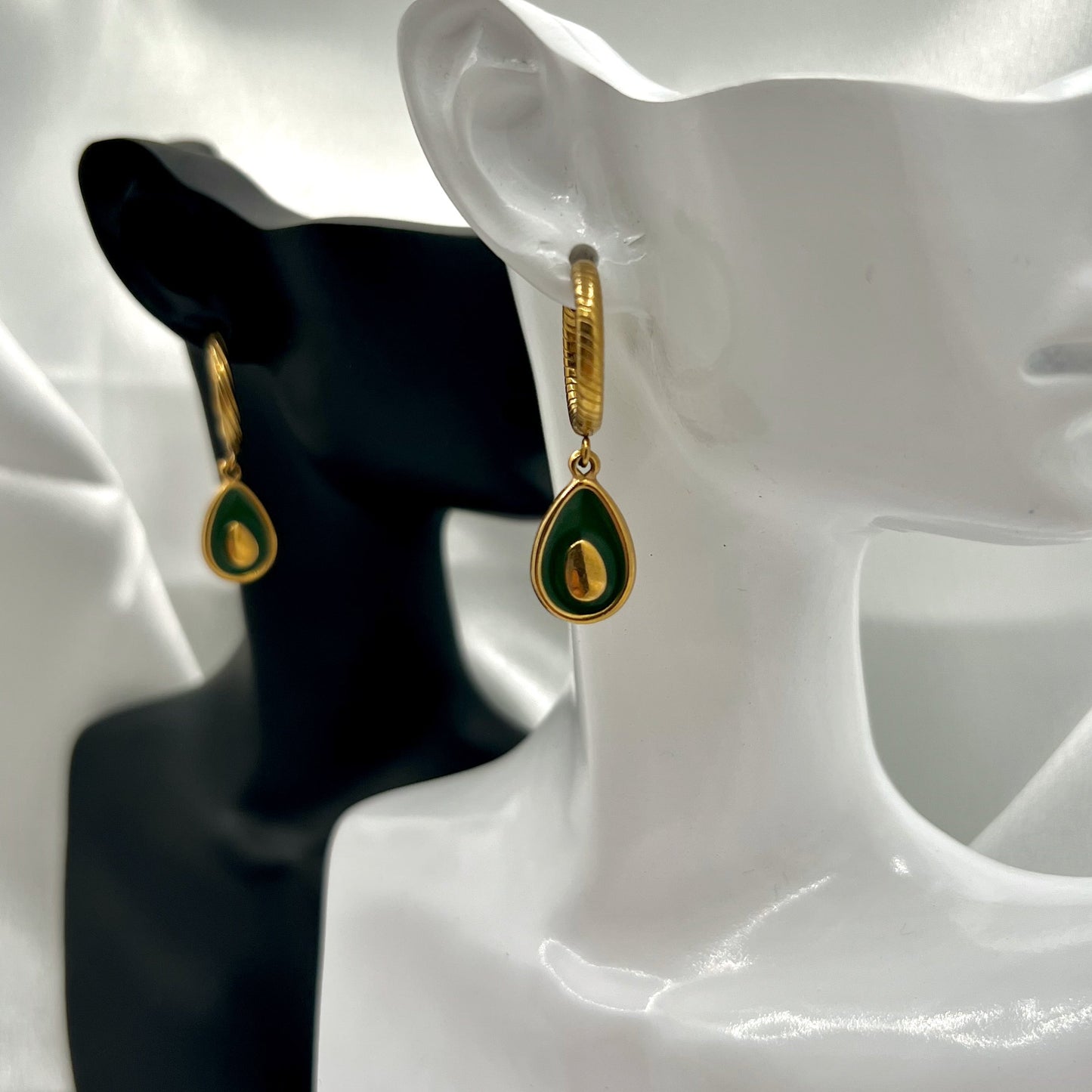 Gold and green avocado earrings on a mannequin bust against a white background