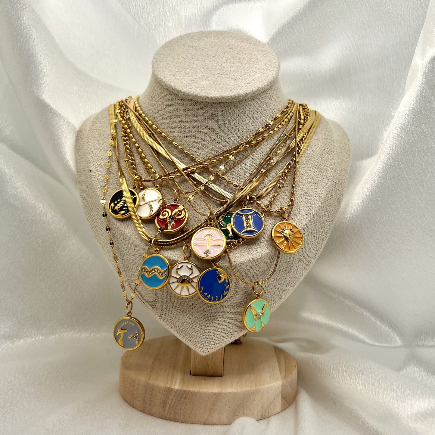 Gold necklace with zodiac pendants on a mannequin bust against a white satin background