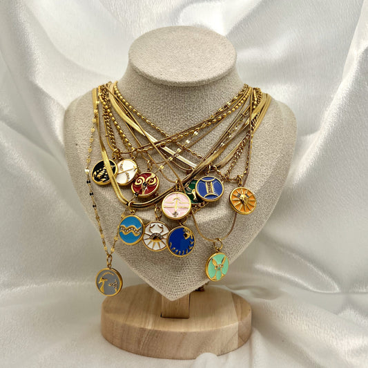Gold necklace with zodiac pendants on a mannequin bust against a white satin background