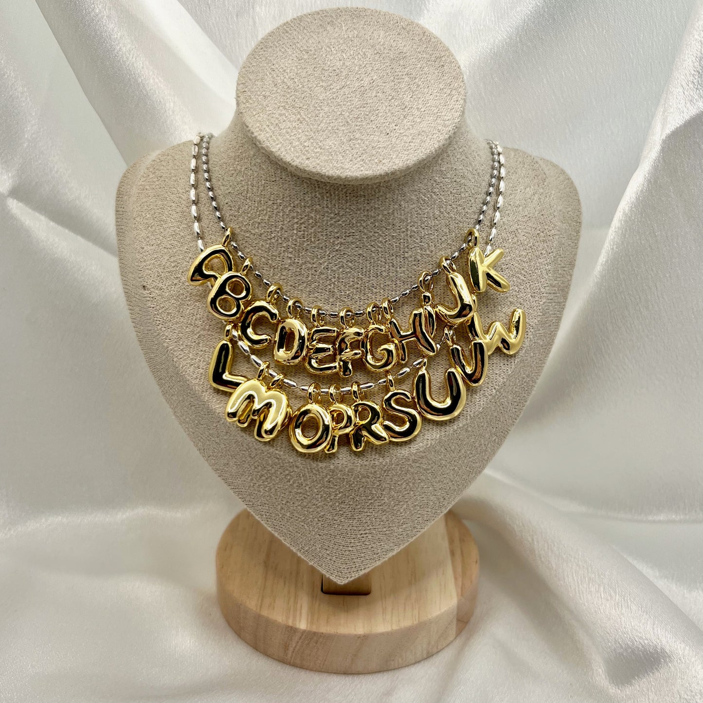 Gold necklace with letter pendants on a beige bust against a white fabric background