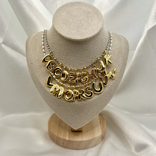 Gold necklace with letter pendants on a beige bust against a white fabric background
