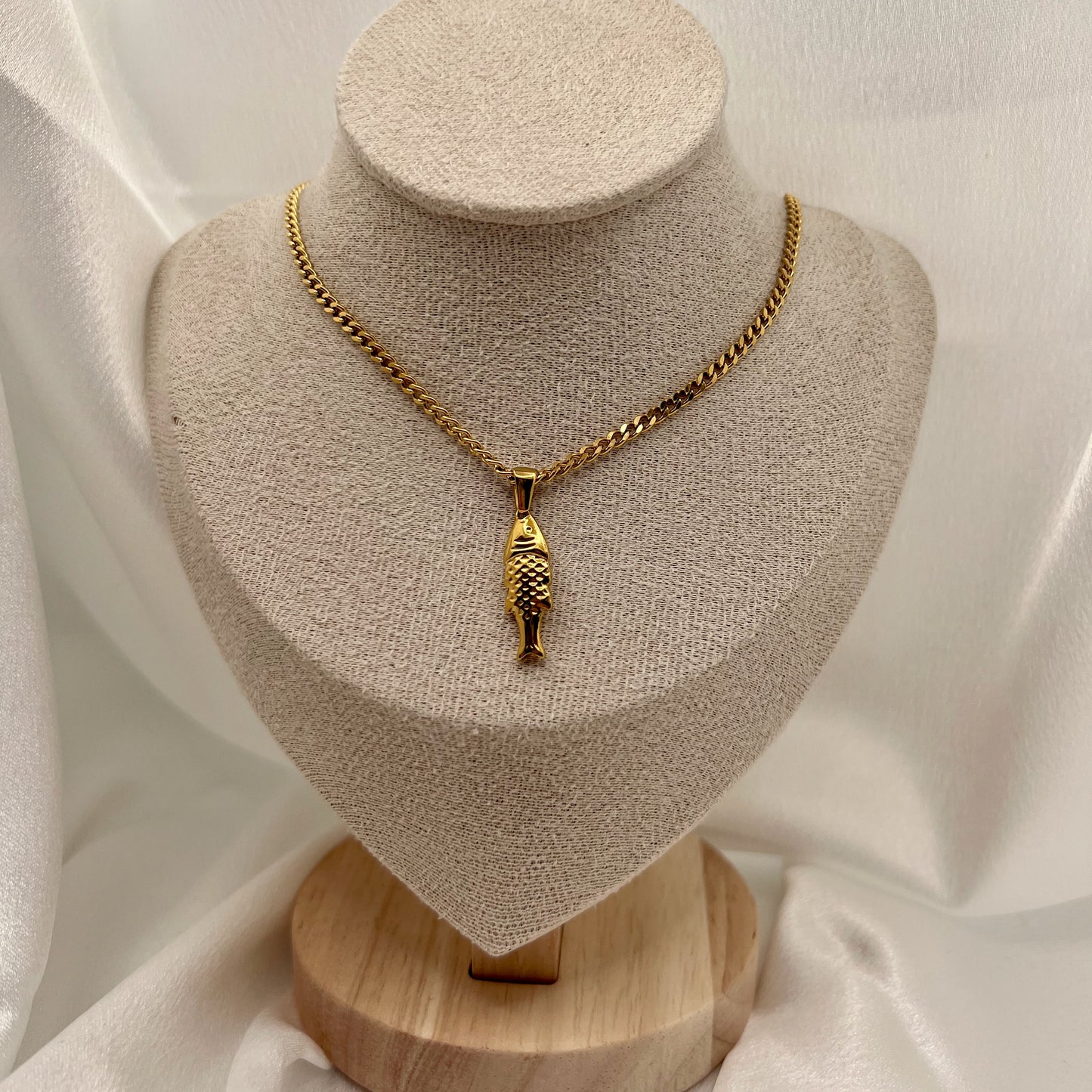 Gold necklace with a fish pendant on a textured stand against a white fabric background