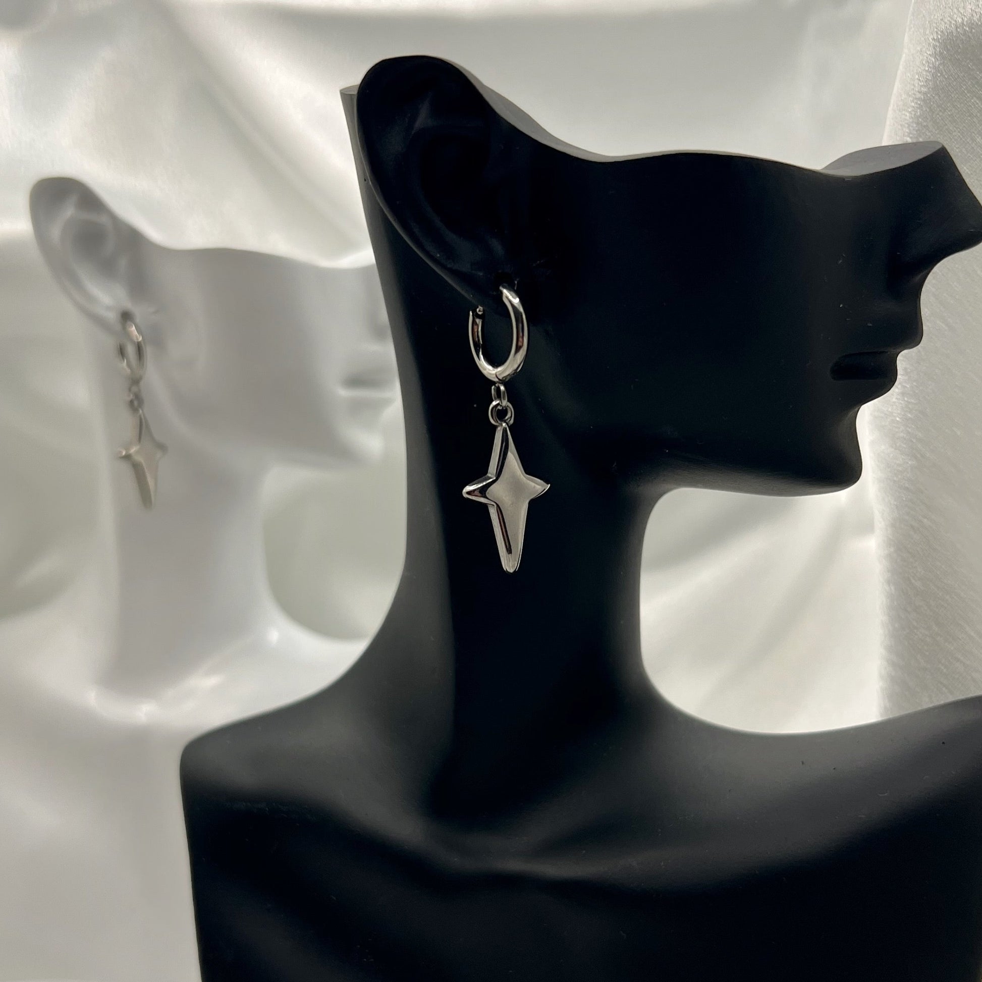 Silver star-shaped earrings on a black mannequin bust against a white fabric background