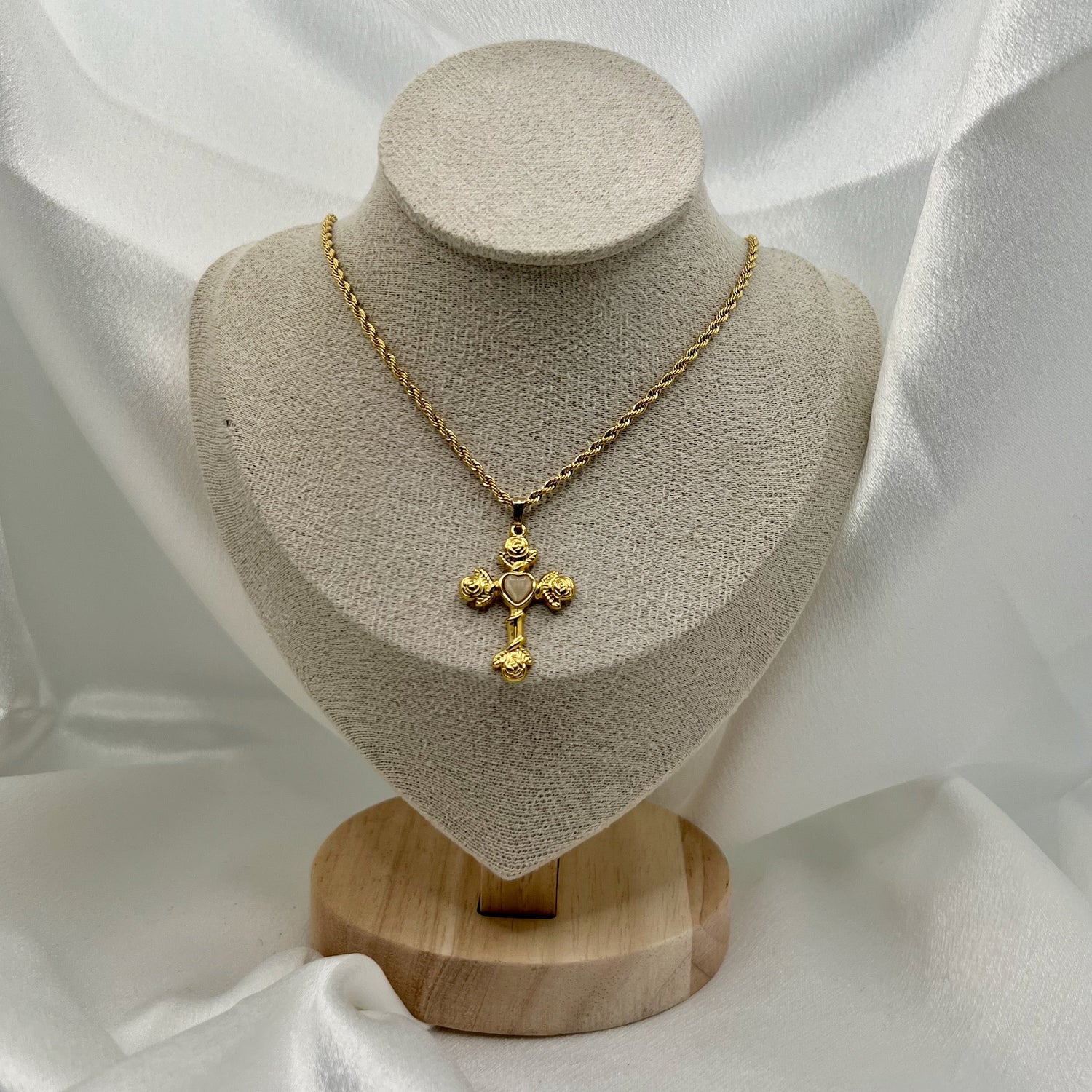 Gold necklace with a cross pendant on a mannequin bust against a white fabric background