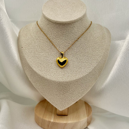 Gold heart-shaped necklace on a beige jewelry display stand with a white fabric background