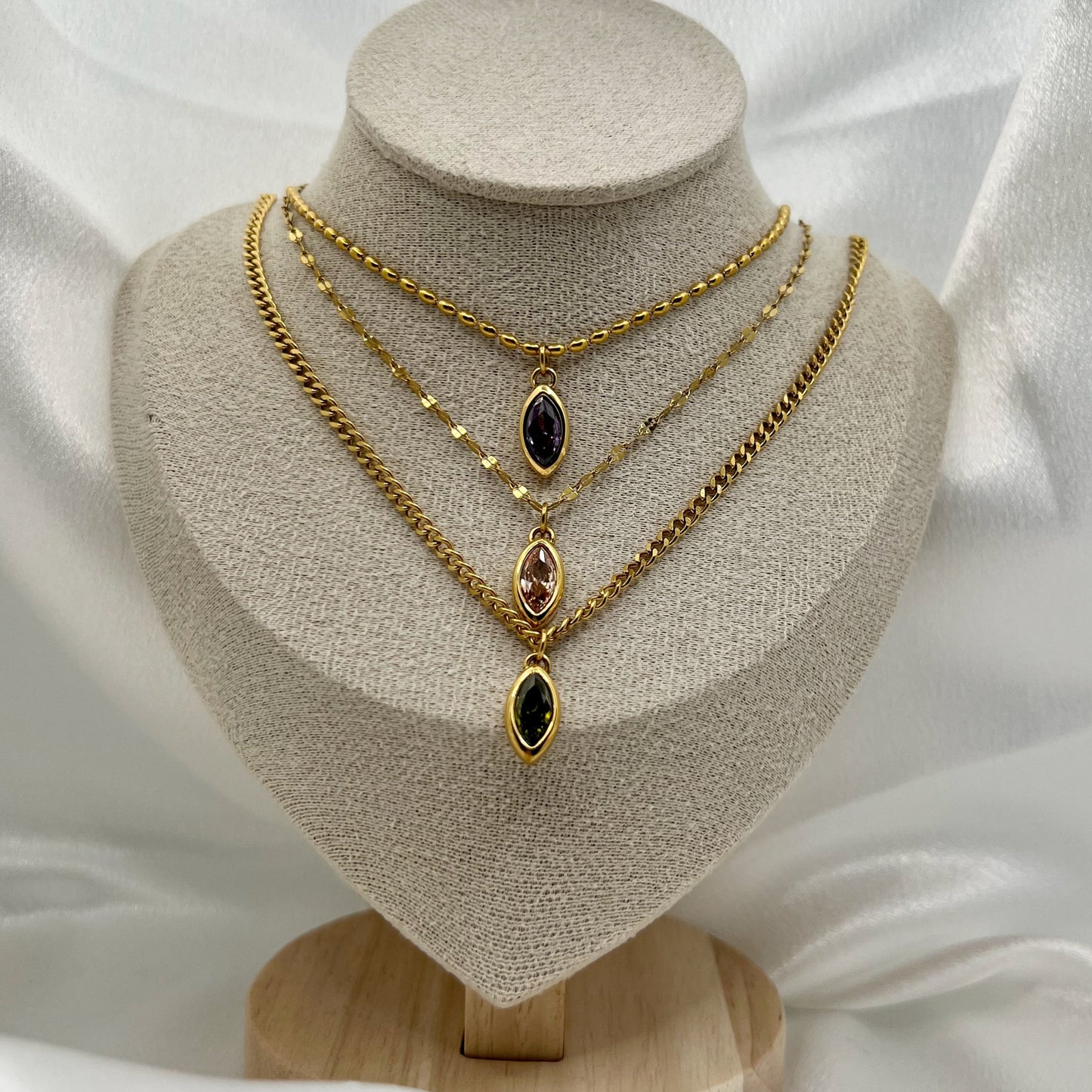 Three gold necklaces with gemstone pendants on a beige mannequin bust against a white fabric background.