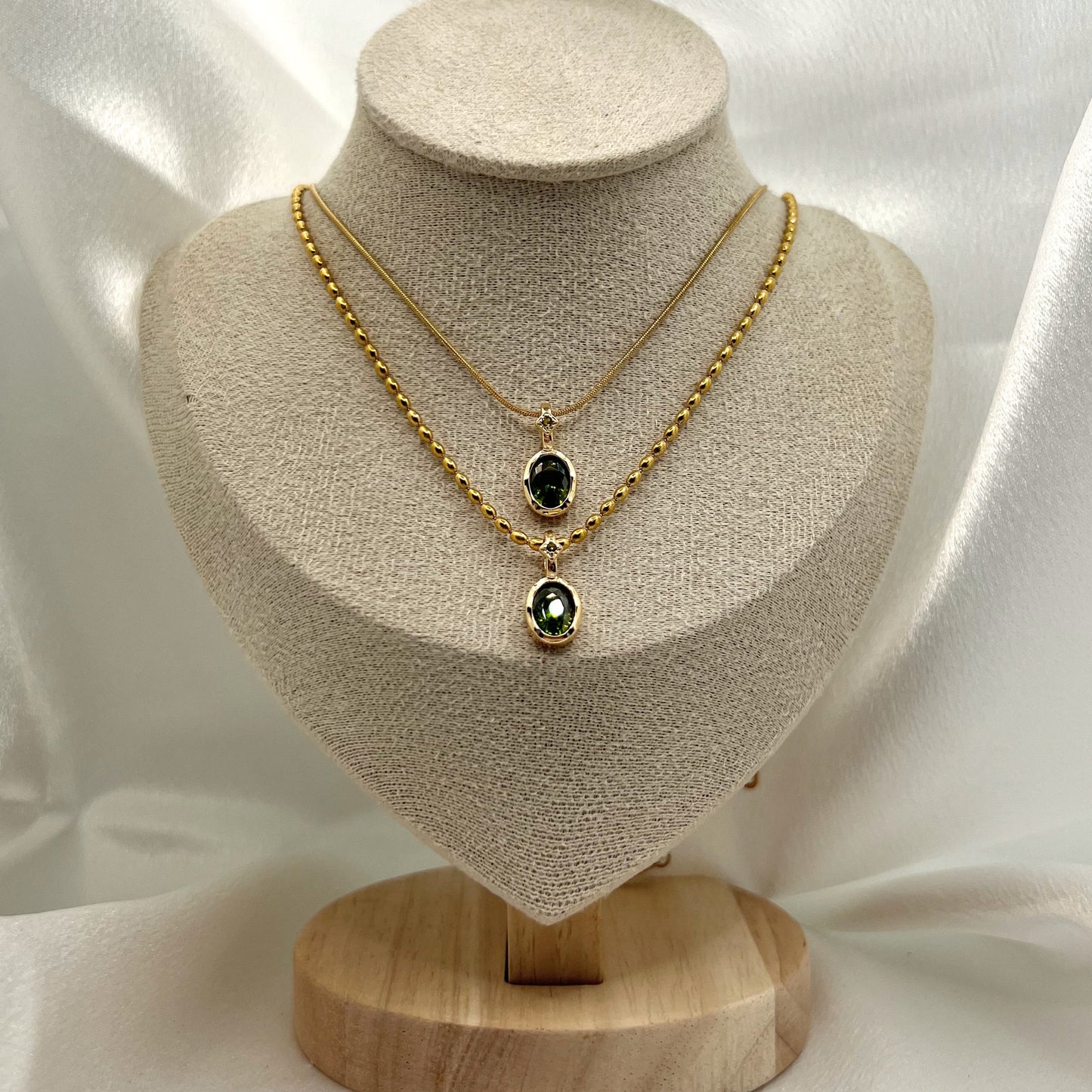 Gold necklace with green gemstones on a beige mannequin bust against a white fabric background