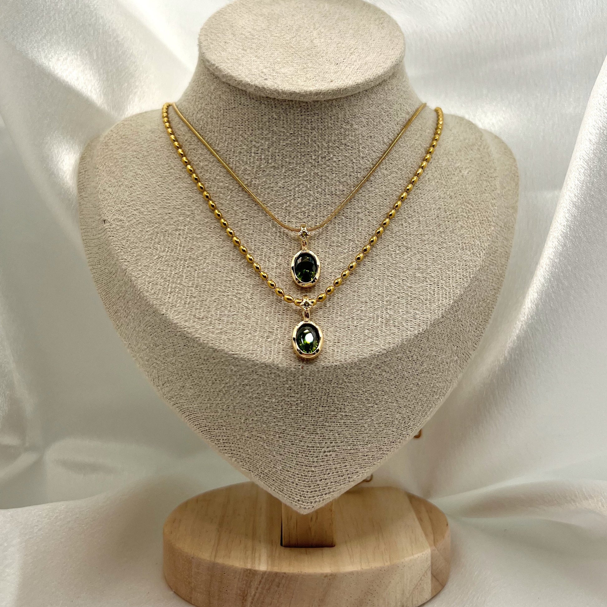 Gold necklace with green gemstones on a beige mannequin bust against a white fabric background